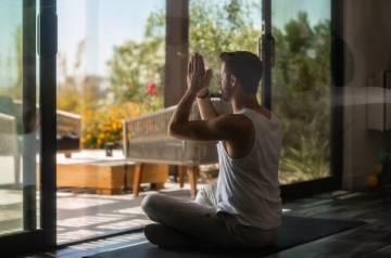 A man practices yoga on a mat in front of a large window at a holistic detox center, promoting relaxation and mindfulness.