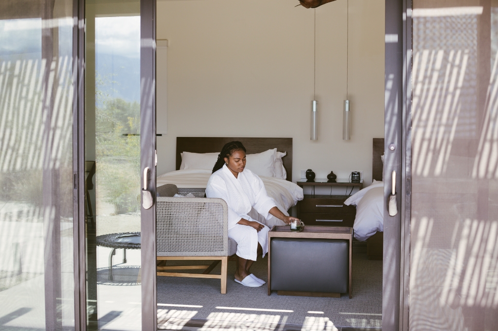 A woman sitting on a bed in a serene room, promoting relaxation at a Colon Cleansing SPA.