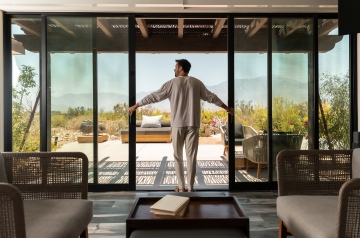 A man stands in front of a sliding glass door at the We Care Spa, looking out into the serene environment.