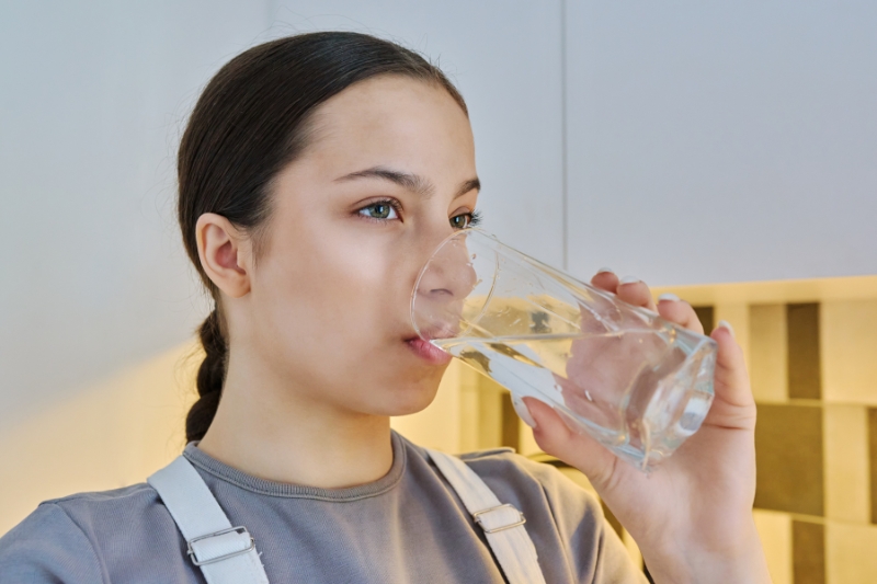 A woman drinking water from a glass, emphasizing the importance of hydration for improving gut health naturally.