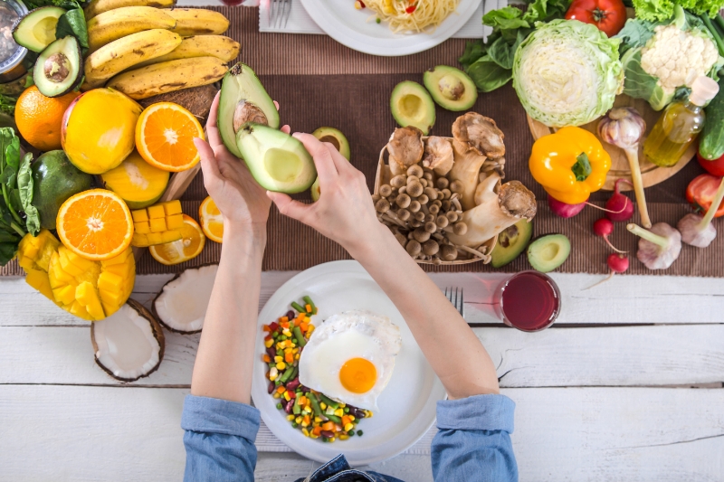 A woman holds an egg and fresh vegetables on a table, promoting fiber-rich foods for improved gut health.