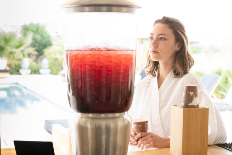 A woman in a bathrobe next to a drink dispenser, illustrating tips for improving gut health by reducing sugar and processed foods.