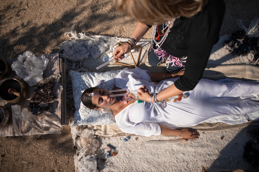 A woman lies on a blanket while another woman performs a holistic body cleanse treatment on her.