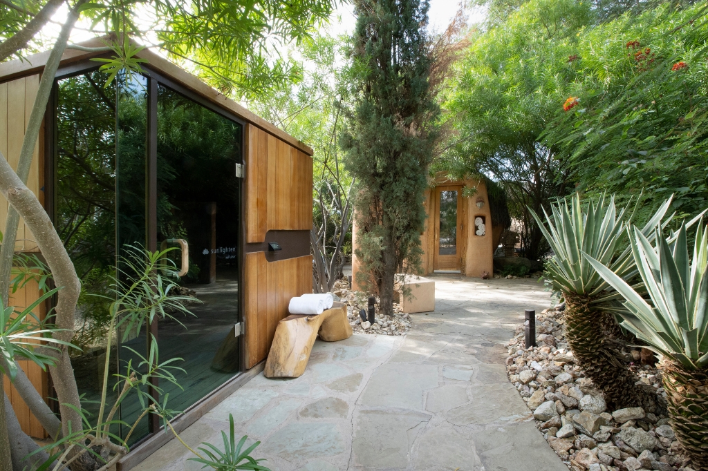 An outdoor sauna nestled in a vibrant garden, part of a serene Holistic Health SPA environment.