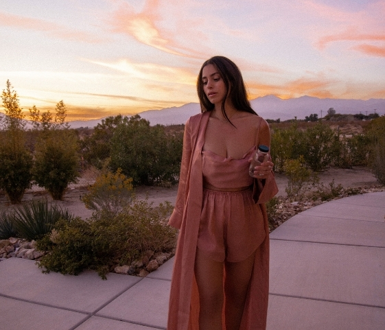 A woman in a pink dress stands on a sidewalk outside the Colonic Retreat, smiling and looking towards the camera.