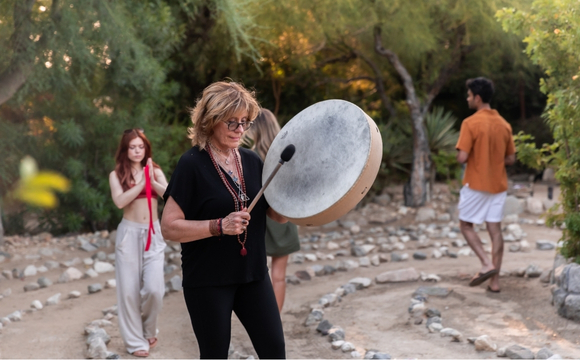 A woman plays a drum surrounded by a circle of rocks at a Colonic Retreat event.