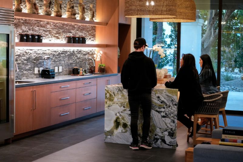 Three people gathered around a modern kitchen counter, discussing or preparing food in a space designed for wellness, with a focus on detoxification and health.