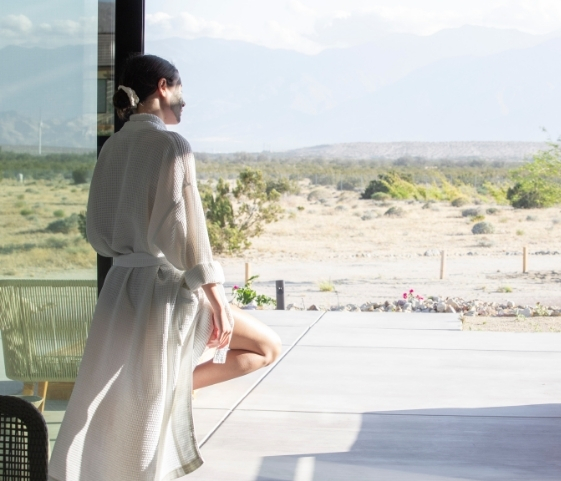 A woman in a robe sits on a patio, gazing at the desert, embodying tranquility during her Holistic Body Cleanse.