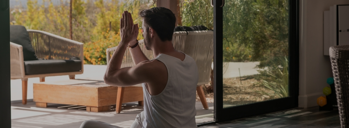 A man practices yoga in front of a sliding glass door, promoting a holistic body cleanse and mindfulness.