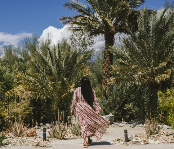 A woman in a pink dress walks gracefully through palm trees, reflecting a peaceful moment at a Holistic Health SPA.