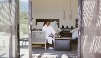 A woman in a robe sits on a bed, embodying tranquility during her 7-night stay at a Juice Fast Detox Retreat.