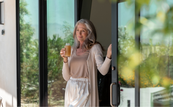 A woman with a glass of beer in hand, standing outside at the Juice Fast Detox Retreat, with trees and sunlight around her.