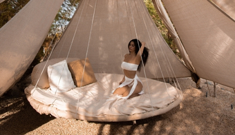 A woman relaxes on a bed inside a luxurious tent at a wellness retreat, enjoying her 7-night stay.