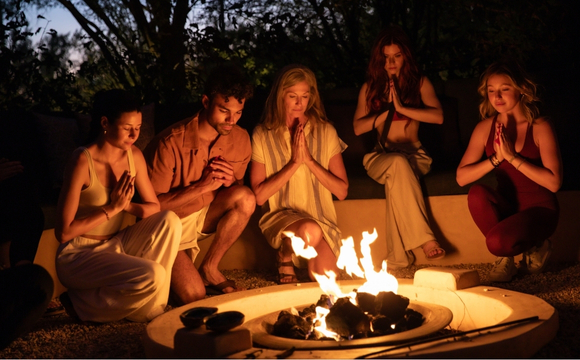 A group of people gathered around a fire pit at a luxury wellness retreat, enjoying a cozy and relaxing atmosphere.