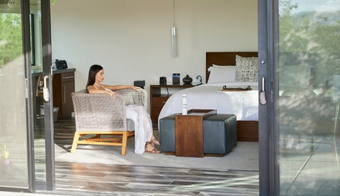 A woman is seated on a bed in a bedroom with sliding glass doors, reflecting a peaceful moment at Wellness Center Palm Springs.