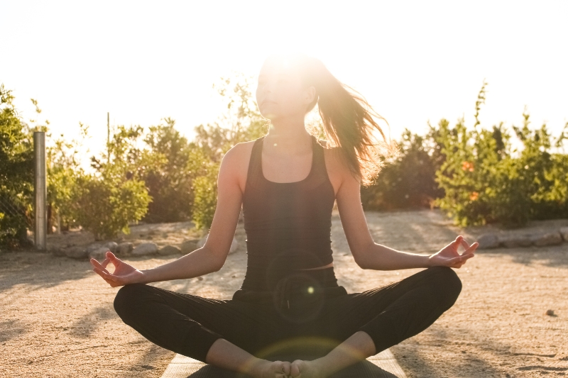 A woman sits in a yoga position, embodying tranquility and focus, promoting energy and mental clarity through wellness practices.