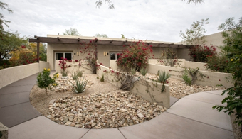 A serene walkway lined with plants and rocks leads to a Colony Suites, promoting a detox cleanse juice fast retreat.