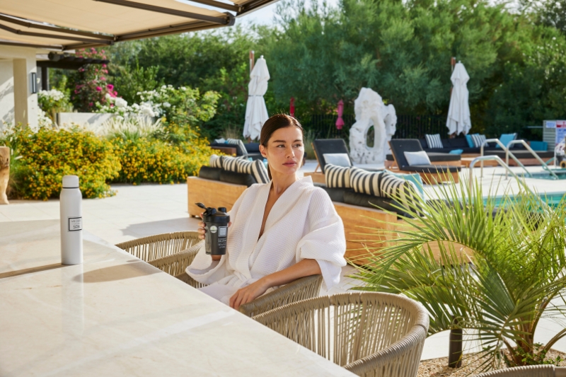 A woman in a robe relaxes at a table by the pool, considering the principles of water fasting.