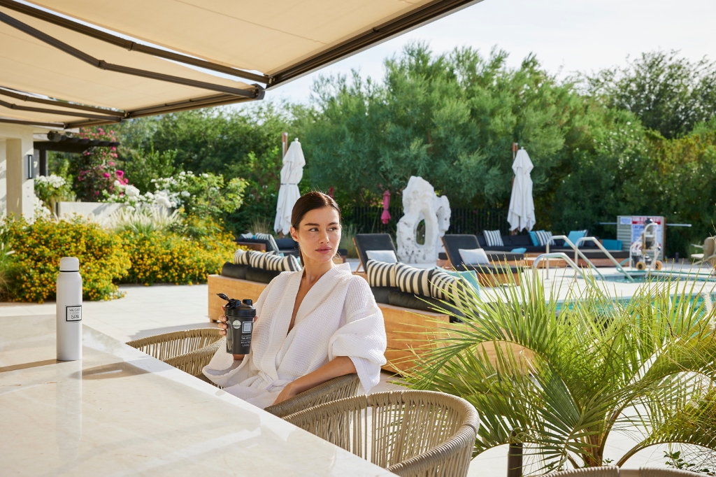 A woman at a table with a juice, representing a Holistic Detox Program atmosphere.