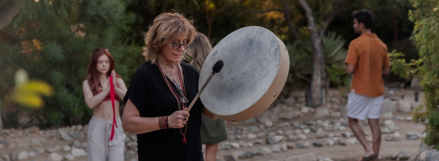 A woman with a drum stands before a group, leading a session for the Holistic Detox Program.