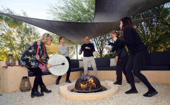 A group of people playing music together around a fire pit during a Holistic Detox Program gathering.
