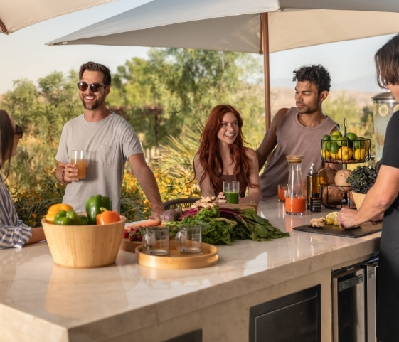 A group of people gathers around a kitchen island, enjoying juices during the Liquid Cleanse Detox program.