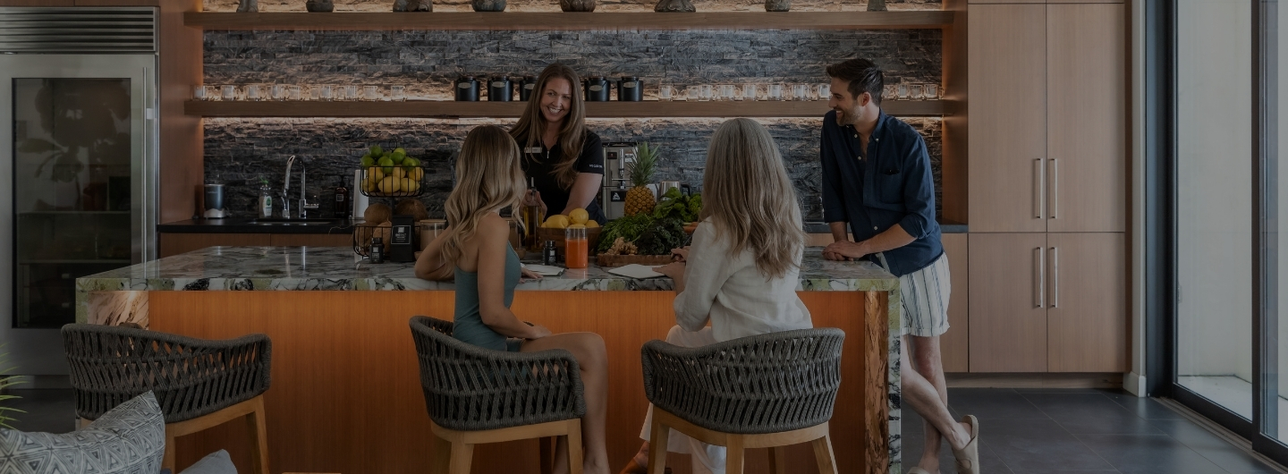A group of people gathered around a kitchen counter, discussing the Liquid Cleanse Detox program.