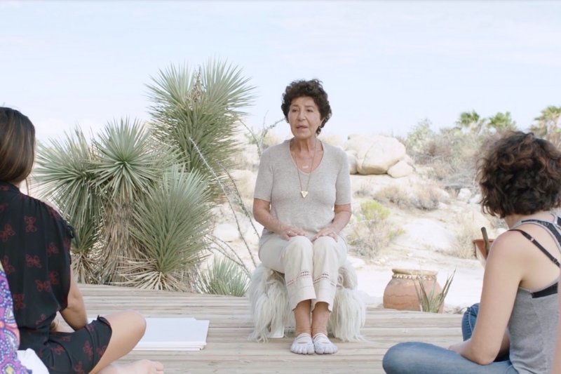 On a wooden deck, a woman talks to three others about autophagy and fasting, part of How We Care Spa's guidance.