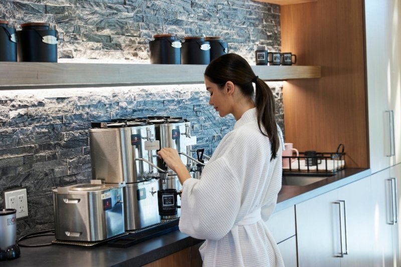 In a kitchen, a woman in a robe brews coffee, emphasizing her morning ritual linked to autophagy and intermittent fasting.