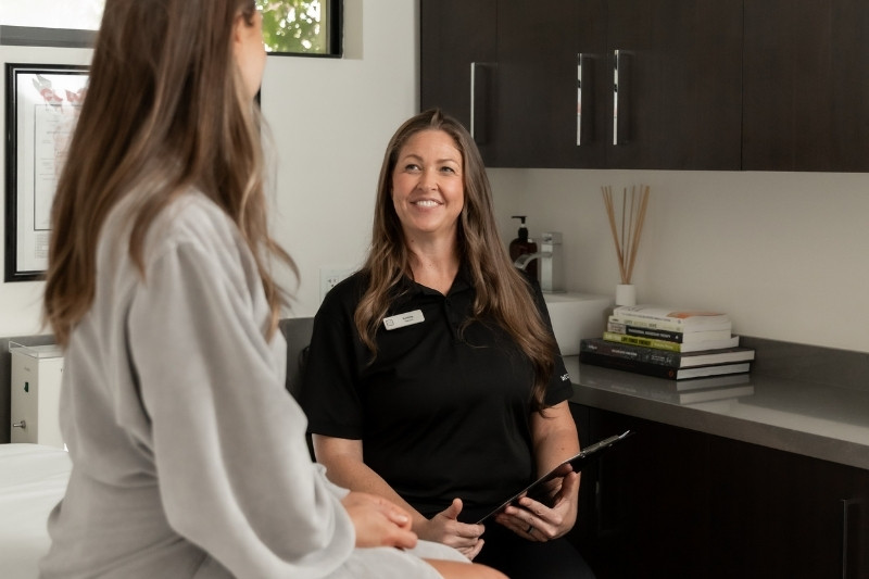 A woman in a chair talks with another woman, focusing on guided fasting and the benefits of colon hydrotherapy.