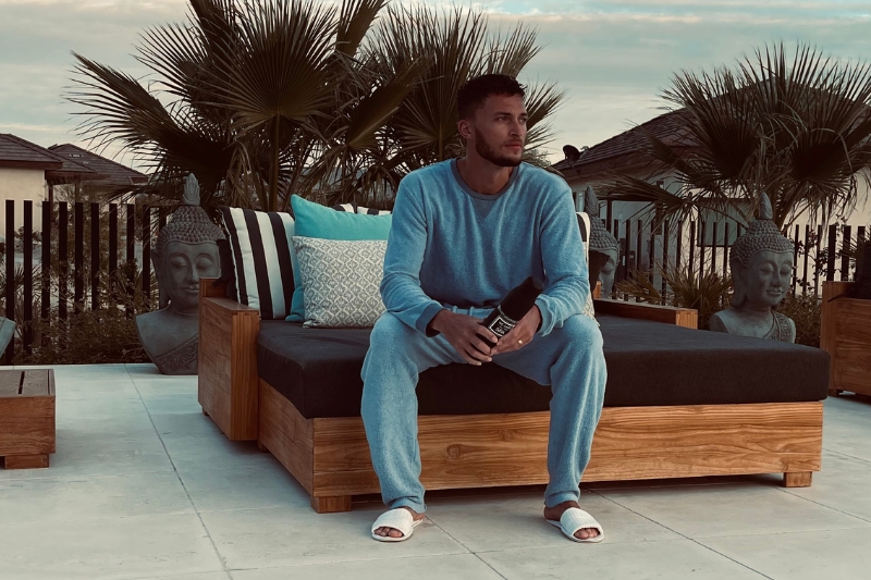 A man on a wooden couch with a bottle of water, embodying a serene moment in the context of preparing for a detox cleanse.
