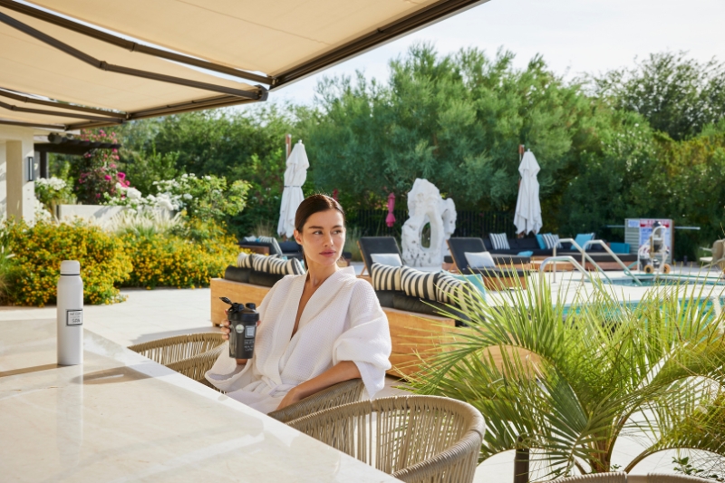 A woman sits at a table with a drink, reflecting on her intentions for a detox cleanse.