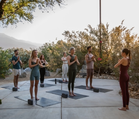 A group of individuals practicing yoga in the desert during a Spiritual Detox Retreat, surrounded by sand and clear skies.
