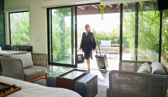 A woman walks through a peaceful room with a bed and sliding glass door, representing a 5-night spiritual detox retreat experience.