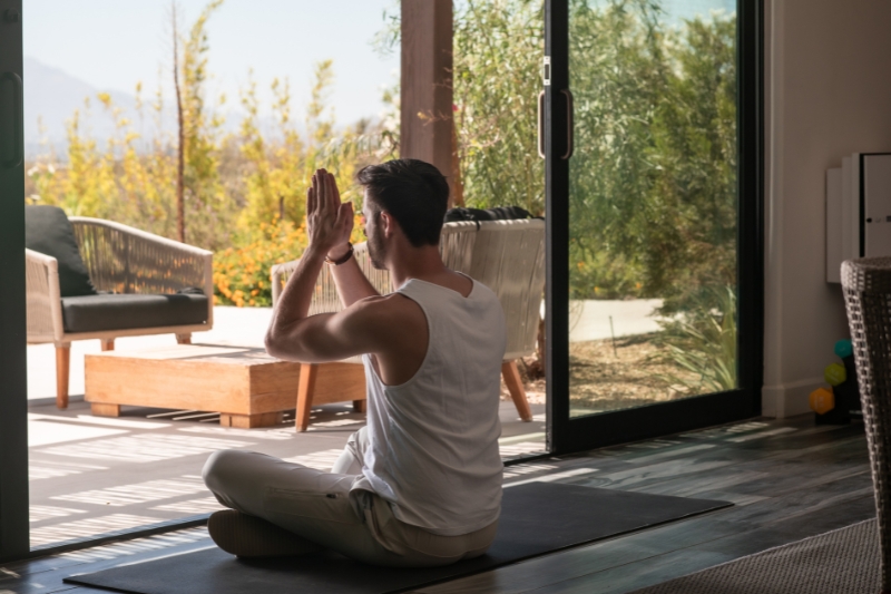 A man practices yoga in front of a sliding glass door, promoting wellness as part of a 7-day weight loss detox program.