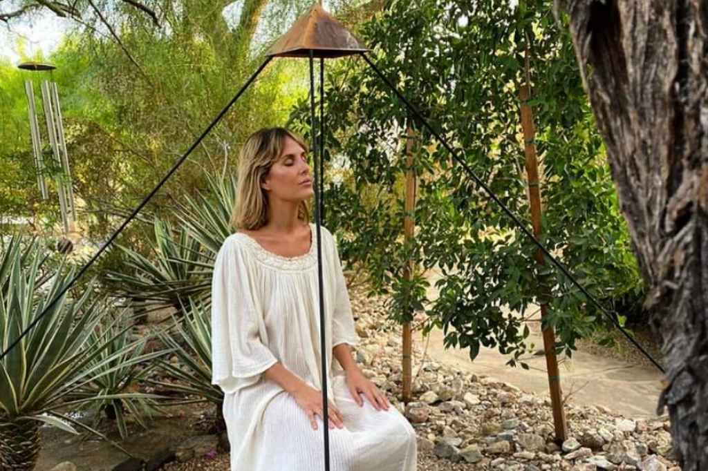 A woman relaxes on a chair beside a tree at a Detox Spa Retreat, surrounded by a serene natural environment.