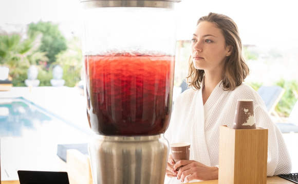 A woman in a bathrobe is next to a large drink machine, which features Liquid Diet Detox retreat.