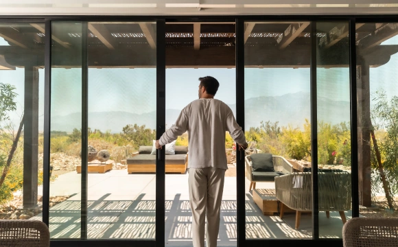 Guest opens patio doors to a peaceful desert setting during an autophagy retreat at We Care Spa