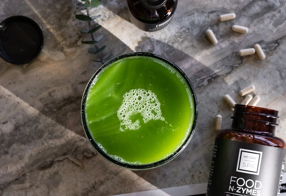 Green juice, Food-Zymes supplements, and capsules arranged on a marble surface for digestive wellness.