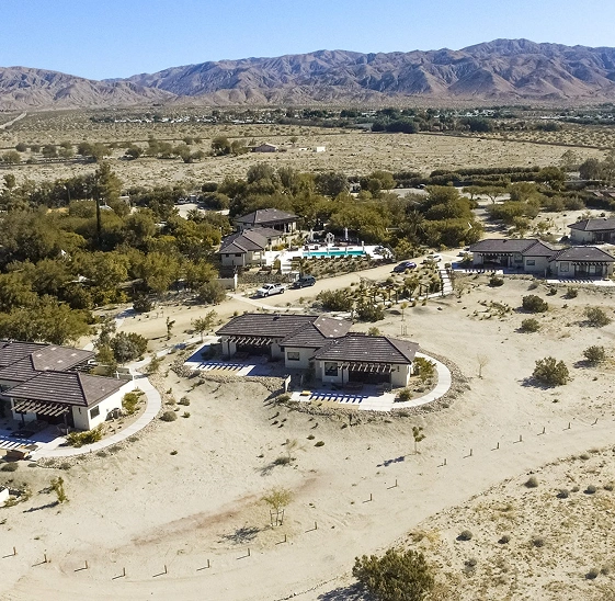 Aerial view of We Care Spa’s expanded desert property with suites, pool, and mountain backdrop.