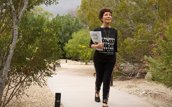 Woman walking through a peaceful garden path at We Care Spa, surrounded by lush greenery.