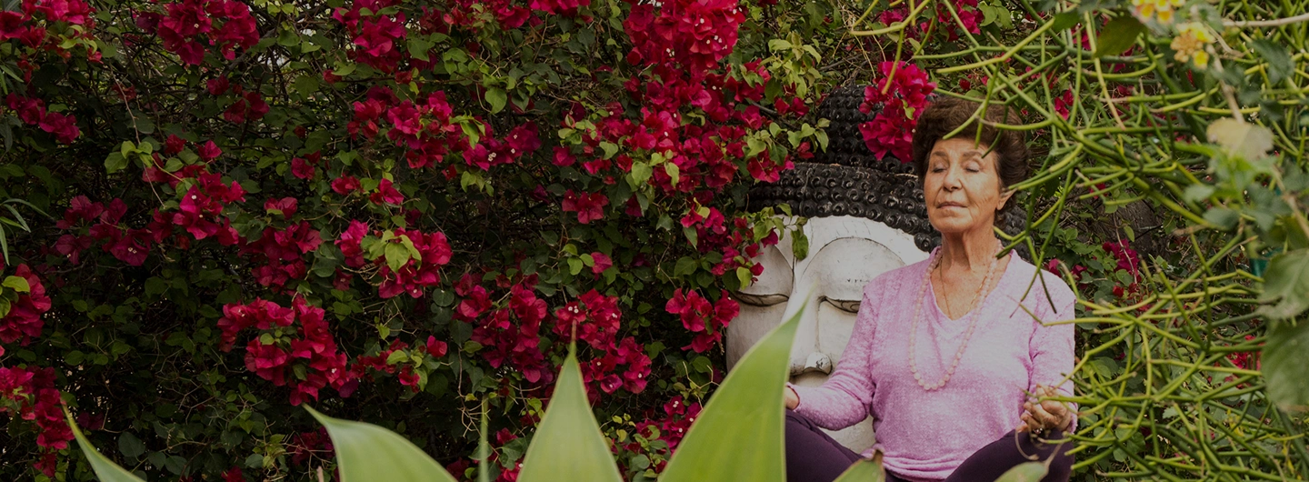 Woman meditating in a vibrant garden, reflecting the wellness story of We Care Spa.